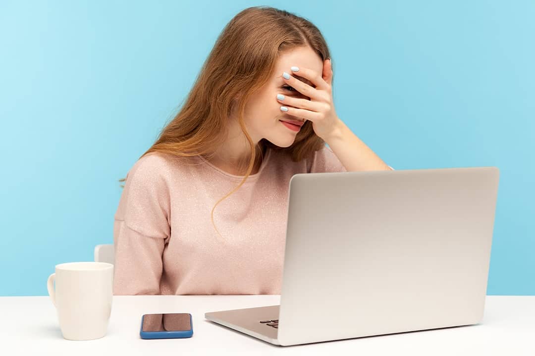 A nervous employee looking at her laptop through her fingers.